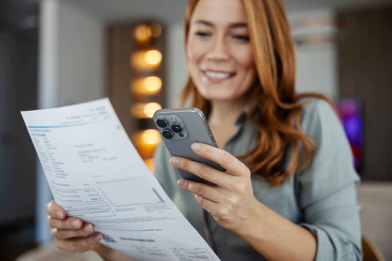 Woman paying securely by phone while holding statement or invoice